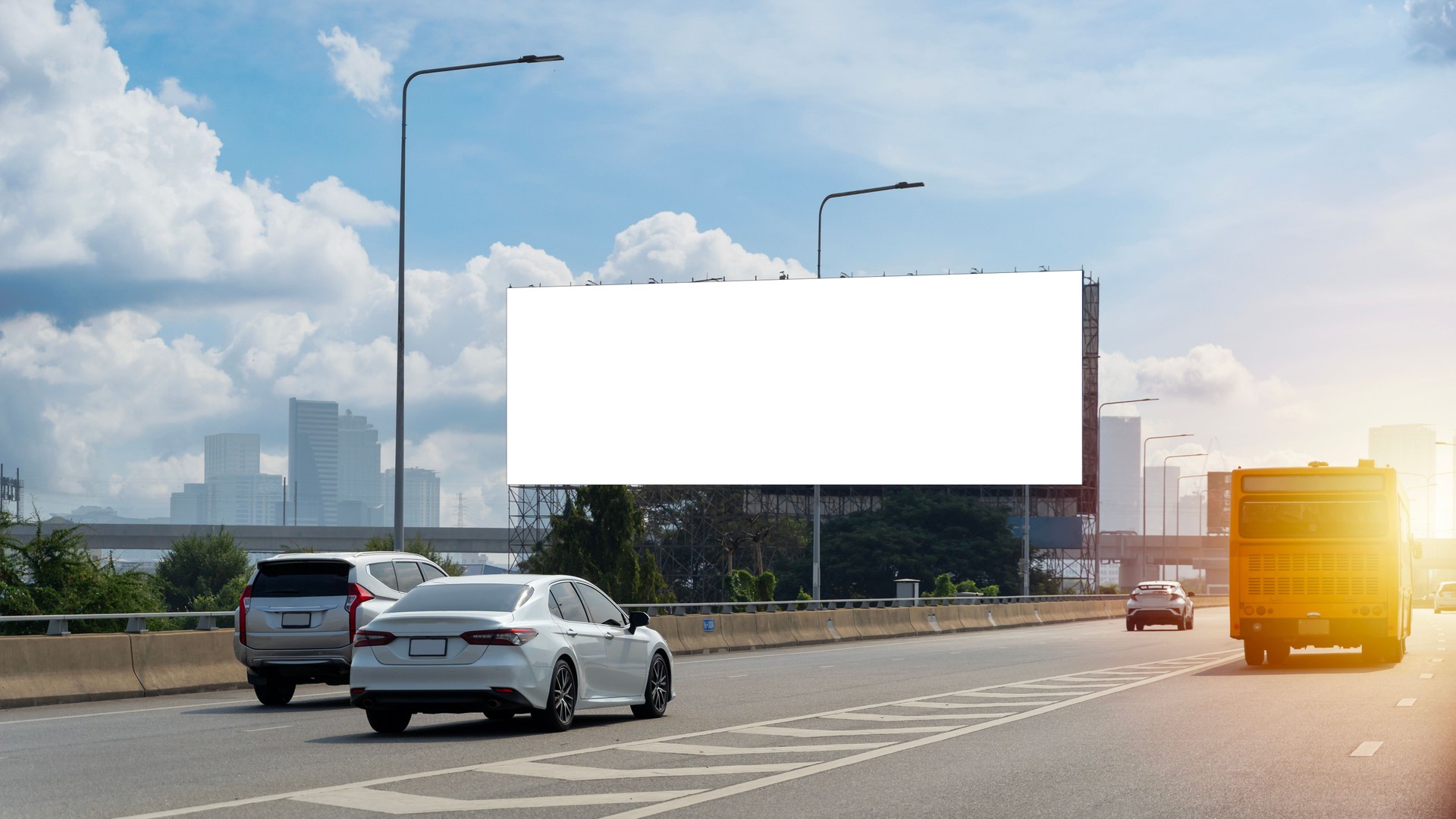 A large, blank billboard on the side of a highway. The billboard is white. It is located in a rural area, with trees and grass in the background.