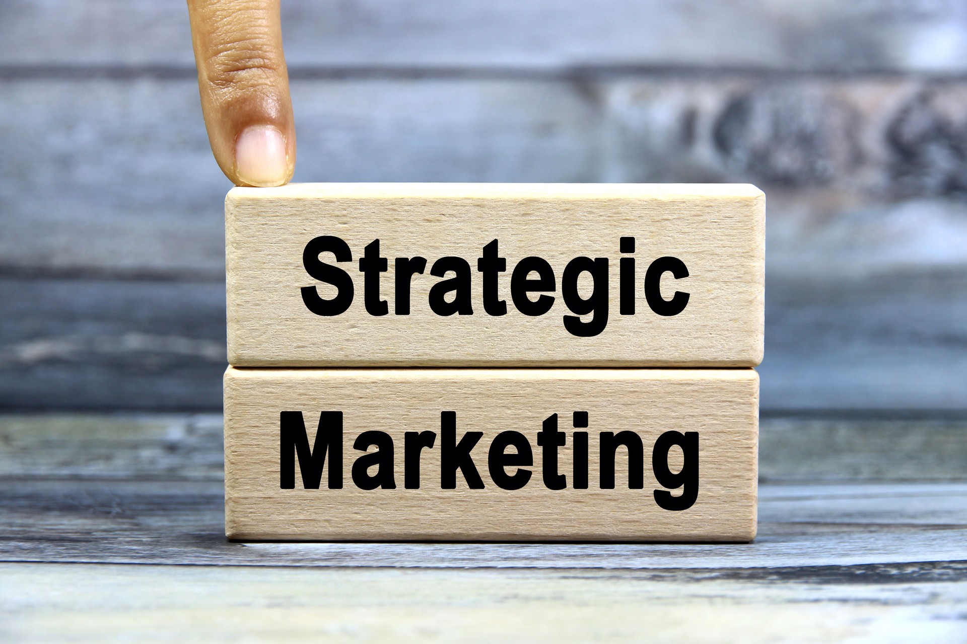 Strategic marketing wording or text on wood block with hand on grey background.Copy space and business concept.