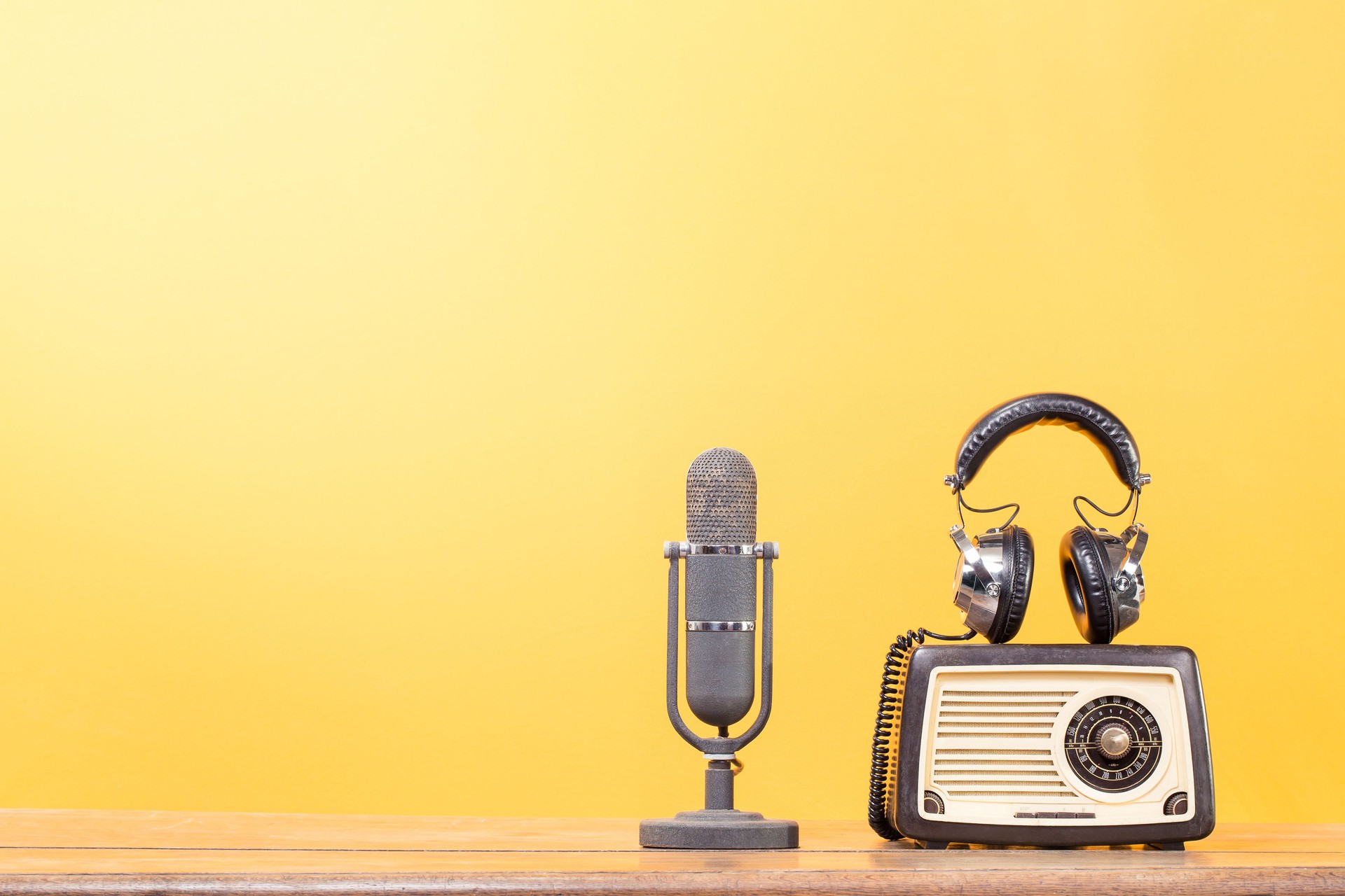 Retro microphone, radio and headphones on the wooden table front yellow background. Vintage style filtered photo
